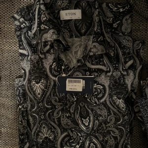 Helt ny Svart och vit mönstrad skjorta från Eton - Snygg skjorta från Eton med ett detaljerat svart och vitt paisleymönster. Perfekt för att ge en stilren touch till din garderob. Skjortan har en klassisk krage .