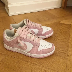 Rosa och vita sneakers från Nike - Snygga rosa och vita Nike sneakers med snörning. Perfekta för en avslappnad stil. De har en klassisk design med en vit sula och rosa detaljer.💞