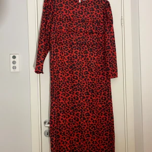 Röd och svart leopardmönstrad vintage klänning i strl 40 från Marcolas Paris - Röd och svart leopardmönstrad vintage klänning i strl 40 från Marcolas Paris.  Klänningen har 3/4 ärm, slits i sidan och fickor i sidorna.   Sparsamt använd och i fint begagnat skick.  Mått Över bröstet: ca 50 cm Längd från axeln och ner: ca 116 cm  Kommer från ett djur och rökfritt hem.