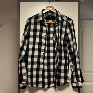 Svartvit rutig skjorta från FSBN - Säljer en stilren svartvit rutig skjorta från FSBN i storlek S. Skjortan har en slim fit passform och är tillverkad i ett lättskött material. Perfekt för både vardag och festliga tillfällen. Den har långa ärmar och knappar framtill. Ett måste i garderoben för en klassisk look!
