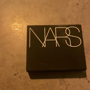 NARS Rouge - Färg Orgasm. Säljer ett superfint rouge från NARS i en snygg, kompakt förpackning med spegel. Färgen är en vacker persikorosa med skimrande finish, perfekt för att ge kinderna en fräsch och glödande look. Perfekt för både vardag och fest!