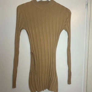Beige ribbad tröja från Missguided - Säljer en stilren beige ribbad tröja från Missguided. Tröjan har en tight passform och långa ärmar, perfekt för kyligare dagar. Den är enkel att matcha med olika outfits och ger en elegant look. Har även en slits på ena sidan 