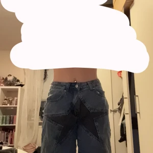 Blå jeansshorts med stjärndetalj - Säljer ett par coola blå jeansshorts med en stor stjärna i mörkare denim. Ny med taggar kvar. Storlek S