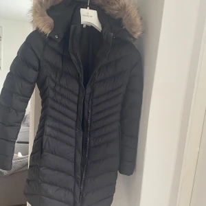 Svart dunjacka från Moncler - Säljer en snygg svart dunjacka från Moncler i mycket bra skick. Jackan har en fluffig pälsdetalj på huvan och en dragkedja framtill. Perfekt för kalla vinterdagar! Storleken är S/P och den är supervarm och bekväm. Passar perfekt för både vardag och festliga tillfällen.