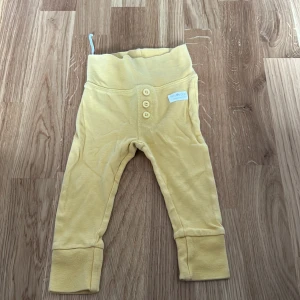 Gula byxor för barn från Tiny One - Säljer ett par söta gula byxor för barn från Tiny One. Byxorna har en bekväm hög midja och dekorativa knappar framtill. Perfekta för små äventyrare!