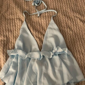 Ljusblå topp med volang - Söt ljusblå topp med volangdetaljer och knytband i nacken. Den har en snygg v-ringad design 