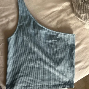 Blå ribbad oneshoulder topp - Säljer en snygg blå oneshoulder topp i ribbat material. Perfekt för sommardagar eller en utekväll. Toppen har en tight passform och är superbekväm att bära. Passar perfekt till både jeans och kjol!