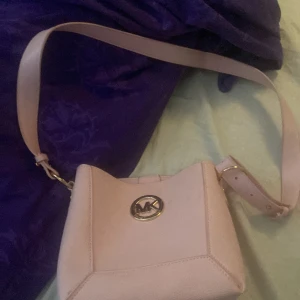 Rosa axelväska med logotypen MK  - Säljer en superfin rosa axelväska med en snygg logotypdetalj på framsidan. Väskan har en justerbar axelrem och en praktisk innerficka med dragkedja. Perfekt för både vardag och fest!, skriv privat om ni vill ha mer bilder på den eller om ni undrar något annat speciellt.💗
