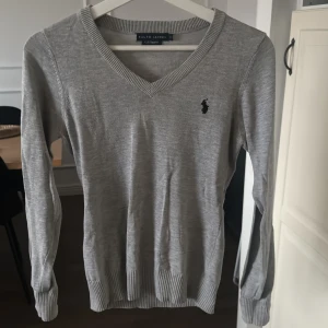 Grå v-ringad tröja från Ralph Lauren - Säljer grå v-ringad tröja från Ralph Lauren. Den är i mycket bra skick och har långa ärmar med ribbade muddar