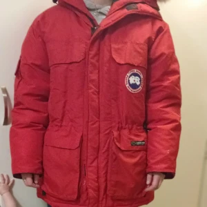 Röd dunjacka från Canada Goose - Säljer en röd dunjacka från Canada Goose med huva och flera praktiska fickor. Jackan har en dragkedja och är perfekt för kalla vinterdagar. Tillverkad i Kanada med högkvalitativt dunfyllning. jackan är I ny skick utan skador eller fläckar, pälsen går att ta av, fler bilder kan skickas, och det finns även ett reg nummer som jag kan skicka bild på som intygar att den är äkta. har säkert glömt något. Den finns I halmstad I fall man bor där och vill komma och testa den osv. Storlek M stor i storlek 