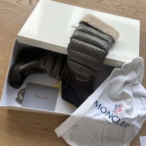 Bruna vinterstövlar från Moncler - Snygga bruna vinterstövlar från Moncler med vadderad grå överdel och mjuk pälsdetalj upptill. Perfekta för kalla dagar med stilren design och varma material.