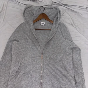 Zara kofta  - Säljer en stilren och bekväm grå hoodie från Zara i storlek L. Den har en praktisk dragkedja framtill och en mysig huva. Perfekt för både vardag och avslappnade tillfällen. Endast använd några gånger och är i nytt skick