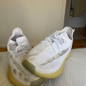 Vita Adidas Yeezy sneakers - Säljer ett par vita Adidas Yeezy sneakers i bra skick. De har en snygg och modern design med en stickad ovandel och en bekväm, ribbad sula i beige. Perfekta för både vardag och fest! Skorna har snörning och är i storlek herr 44