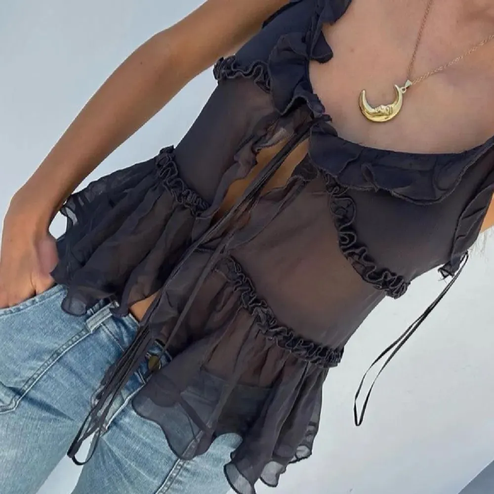 Snygg svart transparent blus med volangdetaljer och knytning framtill. Perfekt för en trendig look. Passar bra till jeans eller kjol.. Yläosat.