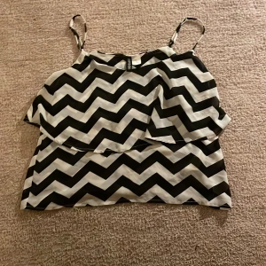 Svartvit mönstrad linnetopp från H&M Divided - Snygg svartvit linnetopp från H&M Divided med ett zigzag-mönster. Toppen har smala axelband och är perfekt för en trendig look. Passar bra till både jeans och kjol.
