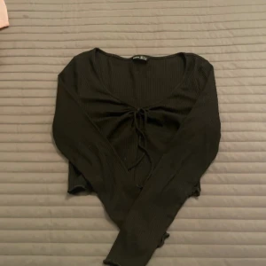 Svart ribbad topp från Shein - Säljer en svart ribbad topp från Shein i storlek S. Toppen har långa ärmar och en snygg knytning framtill som ger en fin detalj. Perfekt för både vardag och fest. Mycket bra skick. 