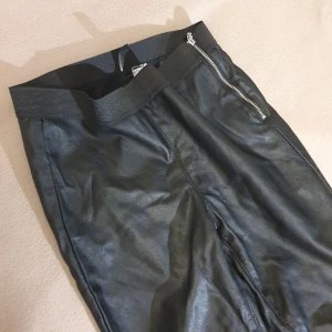 Svarta skinnbyxor med dragkedja - Snygga svarta skinnbyxor i storlek 38. De har en cool dragkedja på sidan och är perfekta för en kväll ute. Byxorna är tighta och ger en stilren look. Mjuk typ borstad insida och stretchig midja så väldigt bekväma Passar bra till både vardag och fest! (PU läder så ej äkta läder) 