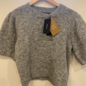 Grå stickad tröja från Vero Moda - Säljer en supermysig grå stickad tröja från Vero Moda. Tröjan har korta ärmar och en rund halsringning. Den är i nytt skick med etikett kvar. Perfekt för både höst och vinter! 🍂❄️