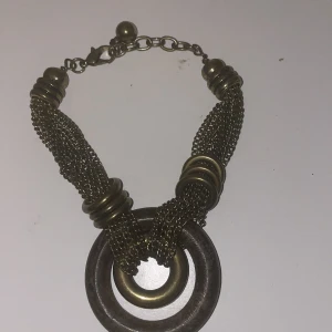 Unikt halsband med metallringar - Säljer ett coolt halsband med flätade kedjor och stora metallringar. Det har en antik finish och en stor cirkulär rund detalj i mitten. Perfekt för att ge din outfit en edgy touch!