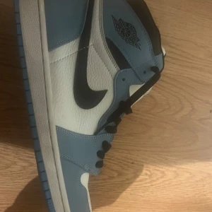 Nike Air Jordans i blått och vitt - Säljer ett par Nike Air Jordans i snygg blå och vit färgkombination. Skorna har en klassisk design med svart swoosh och snörning. Perfekta för både vardag och sportiga tillfällen. De är i mycket bra skick och redo för nya äventyr. Nike unc, universital blue. Det är highs! Inga skador, bra stitch. 