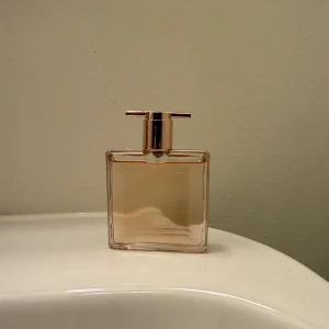 Lancôme Idôle 25ml - Säljer en elegant parfym från Lancôme i en stilren, rektangulär flaska med roséguldfärgad kork. Flaskan rymmer 25 ml men är ca 20 ml kvar och är perfekt för att ha med sig i väskan. Doften är lyxig och tillverkad i Frankrike. Perfekt för både vardag och fest!