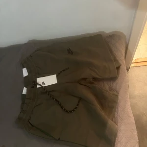 Olivgröna shorts från Nike - Säljer ett par olivgröna shorts från Nike i nytt skick. De har en avslappnad passform med snörning i midjan för justerbarhet. Perfekta för sommarens alla äventyr eller en skön dag på stan. Materialet känns mjukt och bekvämt. Köpt är köpt tar ej tbx 