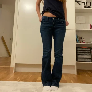 Mörkblå bootcut jeans - Säljer ett par snygga mörkblå bootcut jeans i bra skick. De är lågmidjade och har en klassisk femficksdesign med snygga detaljer på bakfickorna. Perfekta för både vardag och fest! Passar till allt och ger en skön retrovibe.