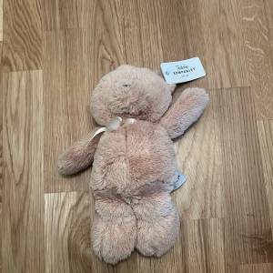 Mjuk nalle från Teddykompaniet - Söt och mjuk nallebjörn från Teddykompaniet i en ljus beige färg. Perfekt som en mysig kompis för barn eller som en fin present. Nallen har en liten rosett runt halsen och är tillverkad av mjukt plyschmaterial.