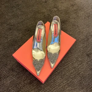 Silvriga pumps från Custommade - Eleganta silvriga pumps från Custommade med spetsig tå och klack. Skorna har dekorativa pärlor framtill som ger en lyxig känsla. Perfekta för speciella tillfällen. Klacken är 6 cm lång. Använda en gång så i väldigt fint skick. 