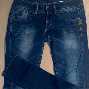 Blå jeans från G-Star - Snygga blå jeans från G-Star med klassisk femficksdesign och knappgylf. Jeansen har en normal passform och är perfekta för en avslappnad stil. Märkesdetaljer syns på både fram- och baksida.