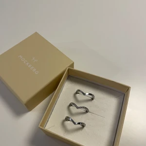 Stilrena silverringar - Säljer ett set med tre stilrena silverringar från Mockberg. Två av ringarna har en enkel, modern design medan den tredje är dekorerad med små glittrande stenar. Perfekta för att bära tillsammans eller var för sig för en elegant look. Passar både till vardags och fest! Säljer alla tre ringar som ett set och Mockberg ask ingår 