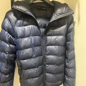 Blå vinterjacka från Peak Performance - Säljer en snygg blå vinterjacka från Peak Performance i mycket bra skick. Jackan har en quiltad design med dragkedja och huva, perfekt för kalla vinterdagar. 