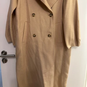 Lång Beige kappa från Zara - Snygg lång beige kappa från Zara med dubbelknäppning och klassisk krage. Stilren design med fickor framtill. Str xs 