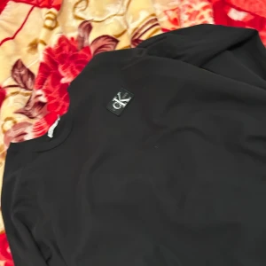 Svart långärmad tröja från Calvin Klein - Snygg svart långärmad tröja från Calvin Klein med en diskret logga på bröstet. Perfekt för en stilren och avslappnad look.