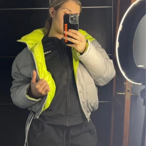 Grå bomberjacka med neongrön insida - Säljer en snygg grå pufferjacka med en cool neongrön insida. Jackan har dragkedja och är perfekt för kyliga dagar. Den har en normal passform och långa ärmar.