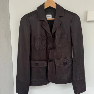 Brun skinnjacka från Boomerang - Säljer en snygg brun skinnjacka från Boomerang i storlek 34. Jackan har en klassisk design med knappar framtill och fyra praktiska fickor. Perfekt för höst och vår, och ger en stilren look. Passar både till vardags och fest!