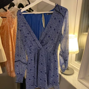 Blå mönstrad klänning från Zara - Säljer en superfin blå klänning från Zara med ett snyggt geometriskt mönster. Den har långa ärmar och en v-ringad design med en liten öppning i bak. Inbyggda shorts!