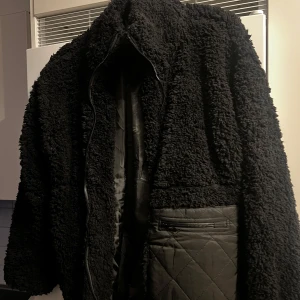 Svart teddyjacka från Boohoo - Mysig svart teddyjacka från Boohoo i storlek 10. Perfekt för kalla dagar med sitt fluffiga material och quiltade detaljer. Jackan har en dragkedja framtill och en innerficka för extra förvaring. Den är både stilren och bekväm, idealisk för höst och vinter. Liten i strl mer som en M 🌸