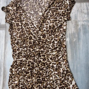 Amisu topp - Snygg topp i leopardmönster med en v-ringning och korta ärmar. Toppen är figursydd och har en lätt rynkad design.