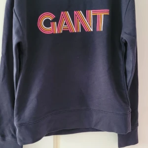 Mörkblå sweatshirt från GANT - Säljer en snygg mörkblå sweatshirt från GANT i mycket bra skick. Den har ett färgglatt GANT-tryck på bröstet i rött, gult och rosa. Perfekt för en avslappnad stil under höst och vår. Passar både till jeans och kjol!