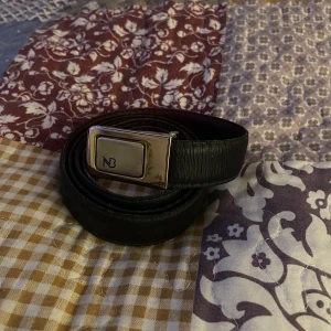 Svart skärp med gulddetaljer - Snyggt svart skärp i skinn med en stilren guldfärgat spänne från märket NB. Perfekt för både vardag och fest. Skärpet har en klassisk design som passar till de flesta outfits. Ett måste i garderoben för den stilmedvetna!
