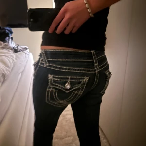 Mörkblå jeans med vita sömmar - Säljer ett par snygga mörkblå jeans med kontrasterande vita sömmar. De har en låg midja och är dekorerade med knappar på fickorna. När jag köpte det stod det att det var true religion, dock inte säker, nästan aldrig använda, köpta för 1300