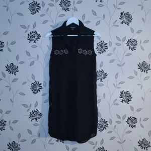 Svart ärmlös blus från Monki, Strl: XS/34 - Snygg svart ärmlös blus från Monki i storlek XS. Blusen har fina broderade detaljer vid bröstet och en klassisk krage. Perfekt för både vardag och festliga tillfällen. Materialet är mjukt och bekvämt, vilket gör den lätt att bära hela dagen.