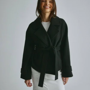 Kappa från nelly  - Har en kappa från Nelly som jag köpte mars 2023, den är i okej skick, inga skador, dock blivit lite ”noppror” typ vid ärmarna. Men som knappt märks. Den heter short belted jacket och finns på Nelly. Vill sälja den då den e något kort för mig, (tycker jag). Den är i storlek xxs/xs