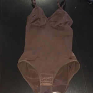 Bodysuit - Säljer en snygg brun bodysuit i storlek S. Den är gjord av 85% polyamid och 15% elastan, vilket gör den både bekväm. Drar in midjan och ger ett ”snatched” resultat . Den har justerbara axelband och en praktisk knäppning i grenen.