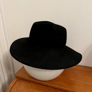 Svart hatt 100% ull - Svart hatt i 100% ull från H&M Divided storlek M/56. Snygg svart hatt i klassisk stil. Perfekt för att ge din outfit en elegant touch. Hatten har en bred brätte och är i mycket bra skick. Passar både till vardags och festliga tillfällen. 