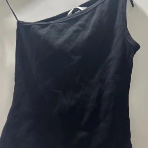 Svart oneshoulder topp - Snygg svart oneshoulder topp i ribbat material. Perfekt för en utekväll eller fest. Den har en stilren design med en axelbandslös stil som ger en modern look. Passar bra till både jeans och kjol.