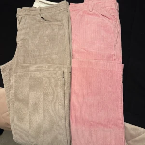 Beige och rosa manchesterbyxor - Två par manchesterbyxor i beige och rosa. De har en klassisk design med fickor och bälteshällor. Perfekta för en avslappnad stil och passar bra till höst- och vårgarderoben. Säljs för 400kr/st