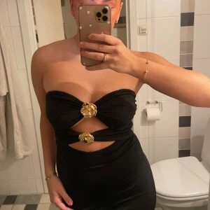 Cutout klänning - En svart cutout klänning med guldiga metallblommor. Så modern! Står ej storlek men gissar på en M!  Aldrig använd! 💓