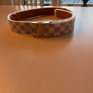 Rutig bälte  - Säljer ett snyggt bältr i rutig design med en elegant guldspänne. Bältet är i nytt skick och har en stilren kombination av beige och grå färger. Perfekt för att lyfta din outfit till nästa nivå!